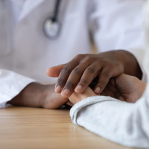 Young woman holding hands of african american male doctor, feeling appreciate for serious illness treatment close up. Mixed race hopeful doc comforting, supporting millennial desperate female patient.